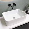 A white ceramic bathroom sink with a stainless steel drain strainer and a black faucet mounted on a light gray wall.
