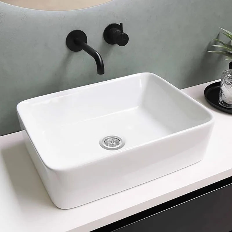 A white ceramic bathroom sink with a stainless steel drain strainer and a black faucet mounted on a light gray wall.