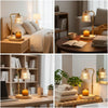 A dimmable electric candle warmer lamp with a glass bulb sits on a wooden surface next to stacked candles.