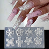 A hand displays a manicure with sheer pink and white floral silicone nail art molded designs.