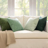 A collection of olive green and sage colored corduroy throw pillow covers arranged on a light beige sofa near a window.