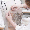 Hands are pinning fabric onto a dress form using carbon steel T-pins for sewing or knitting.