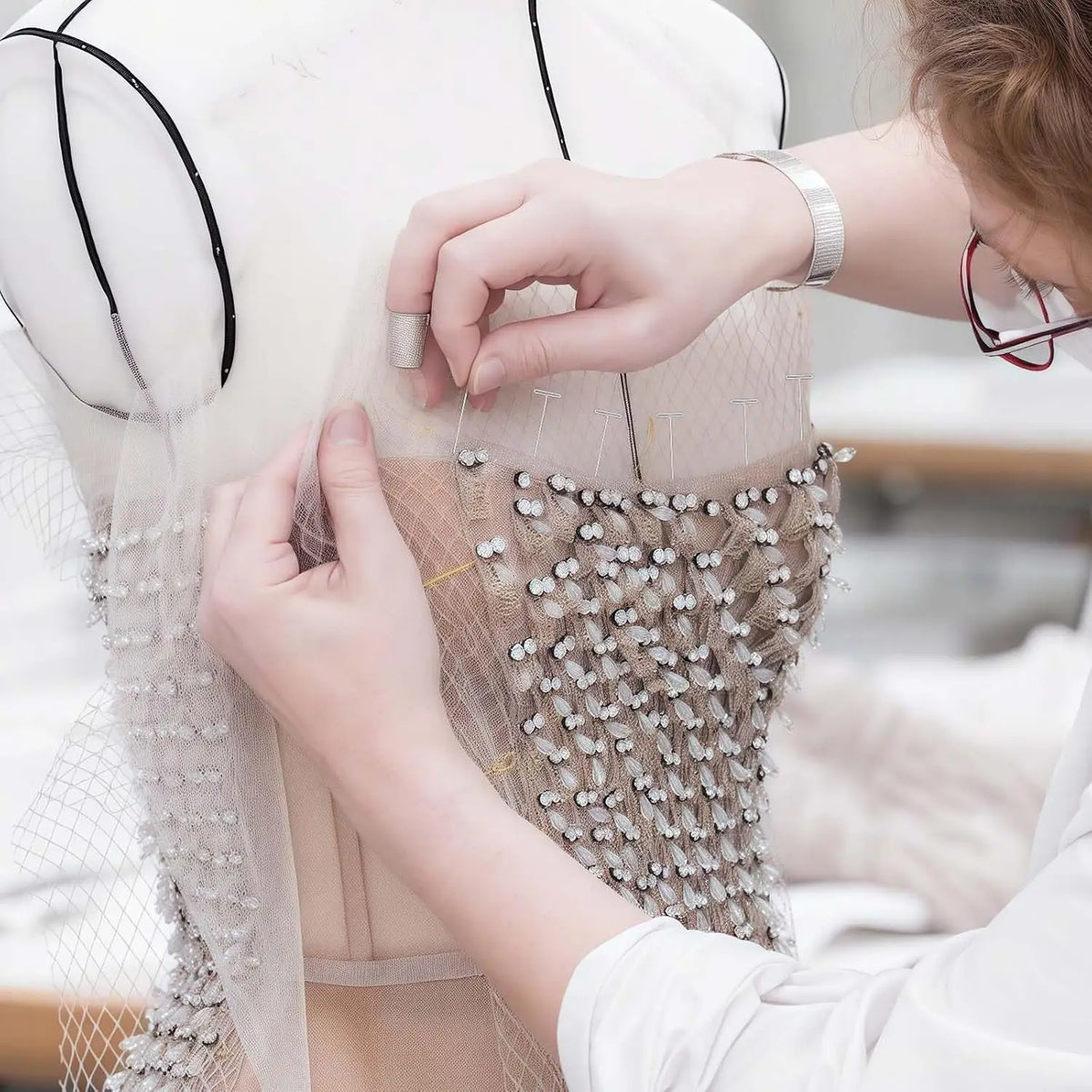 Hands are pinning fabric onto a dress form using carbon steel T-pins for sewing or knitting.