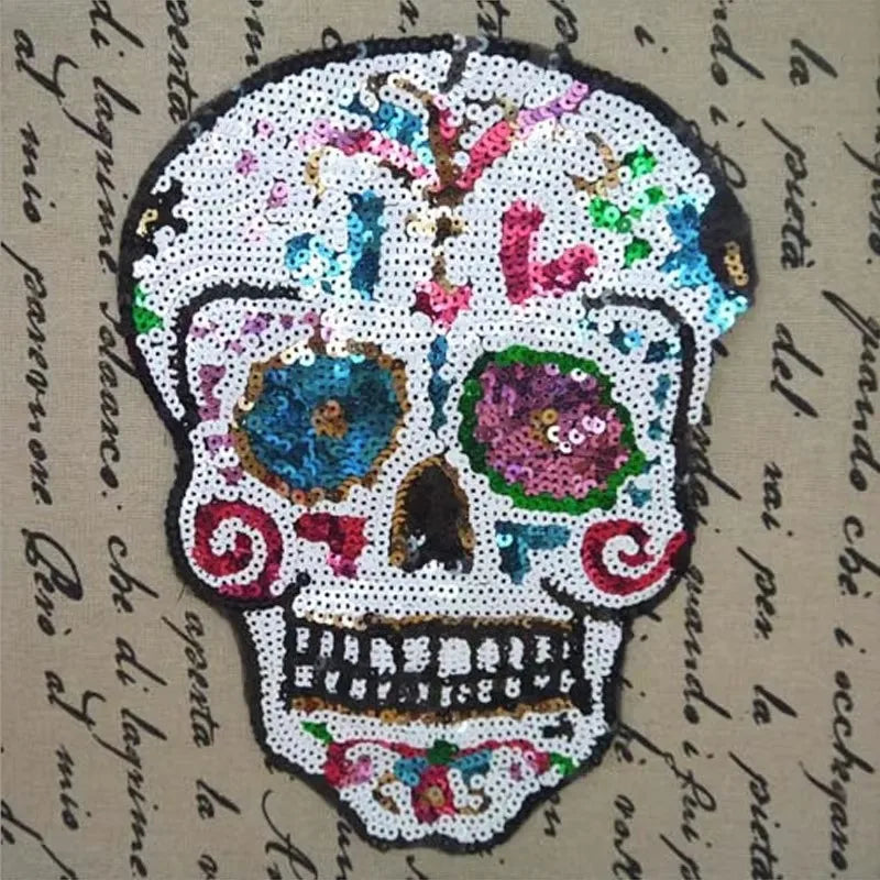 A white sequin skull embroidered patch featuring colorful floral and decorative elements on a beige fabric background.