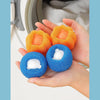 A hand holds several orange and blue reusable laundry balls for washing machine cleaning.