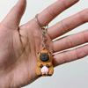 A small brown capybara charm keychain is being held between fingers.