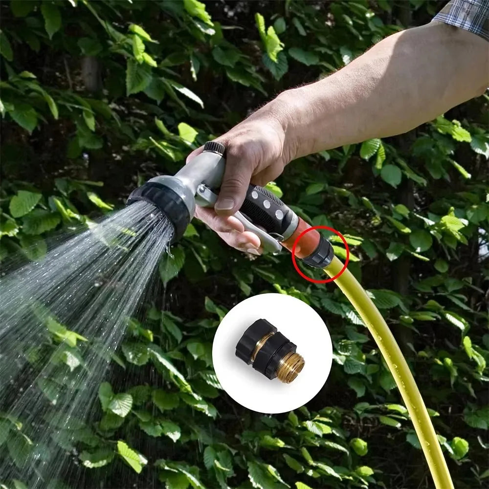 A hand sprays water from an aluminum garden hose quick connector set onto green foliage.
