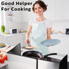A woman wearing an apron is preparing food on a stovetop with a foldable stainless steel splatter guard.