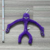 A purple plush toy shaped like a bird with a long body and small feet is displayed against a wooden background.