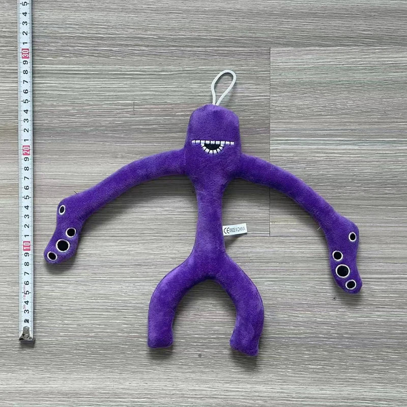 A purple plush toy shaped like a bird with a long body and small feet is displayed against a wooden background.