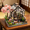 A detailed miniature Japanese sakura tea house model kit featuring a dark wooden structure and pink blossoms on a wooden disp