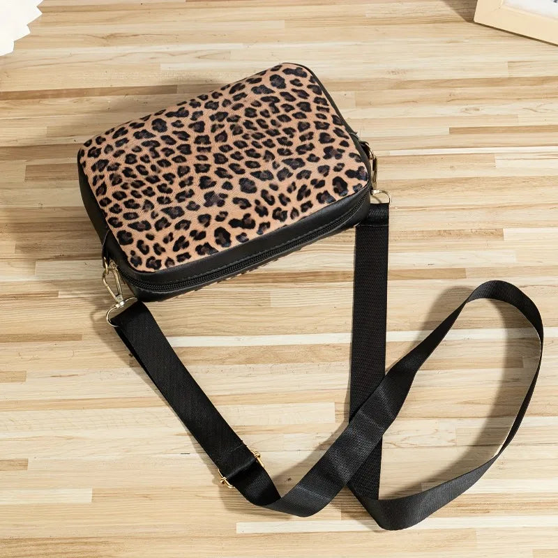 A leopard print crossbody bag with a black strap resting on a light wooden surface.