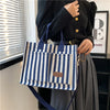 A woman holds a blue and white striped canvas tote bag with inner pockets against a window backdrop.