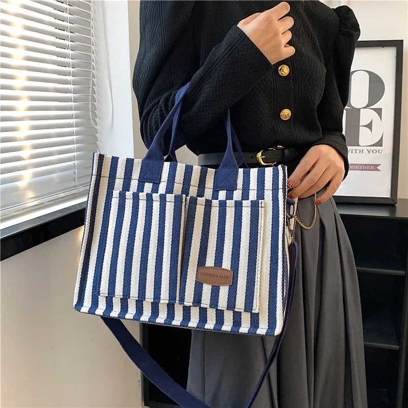 A woman holds a blue and white striped canvas tote bag with inner pockets against a window backdrop.