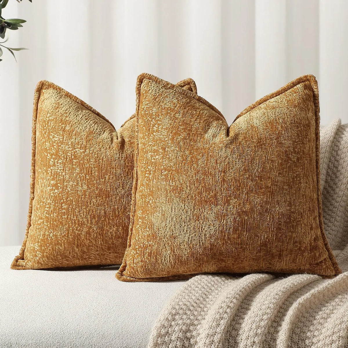 A square, textured, golden brown chenille decorative cushion cover resting on a light-colored sofa.