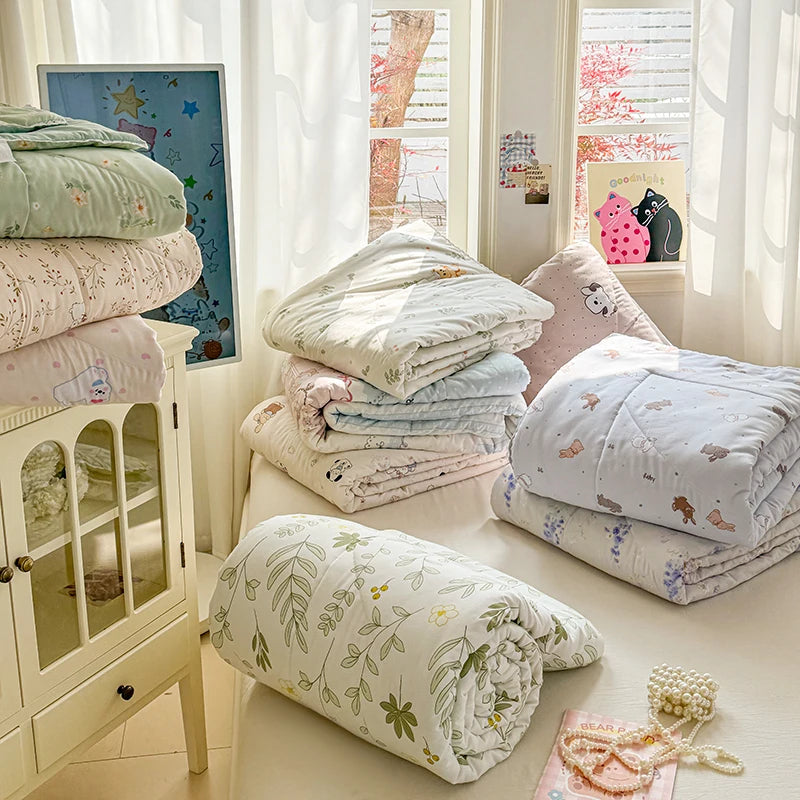 A stack of white and floral patterned bedding, including a duvet and pillows, is displayed next to a white cabinet.