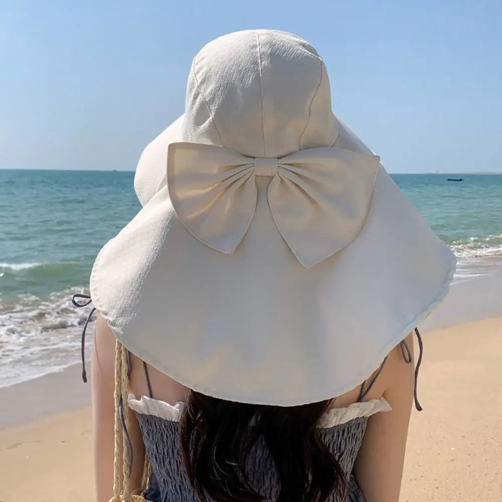 Eine Frau mit breiter Sonnenhut und Schleife blickt über den Ozean am Strand.