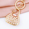 Gold-toned handbag keychain featuring white pearls and pink crystal rhinestones on a soft pink fabric background.