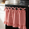Red and white plaid farmhouse oven skirt with ruffled trim hanging on a black stove rack