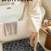 A woman stands beside a bathtub with a pebble bath mat placed on the floor.
