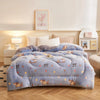 A light blue plush throw blanket with a floral pattern is displayed on a bed, next to a bedside lamp and framed art.
