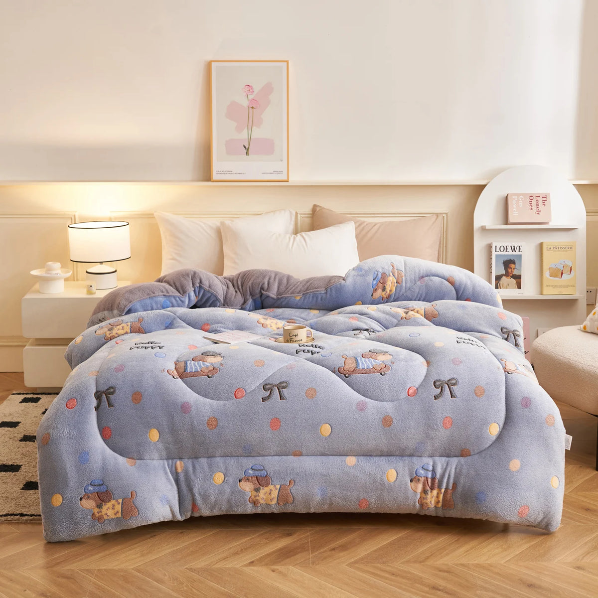A light blue plush throw blanket with a floral pattern is displayed on a bed, next to a bedside lamp and framed art.