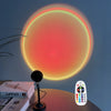 A USB sunset projection light is shown illuminating a wall with a bright orange glow, next to a remote control and some books
