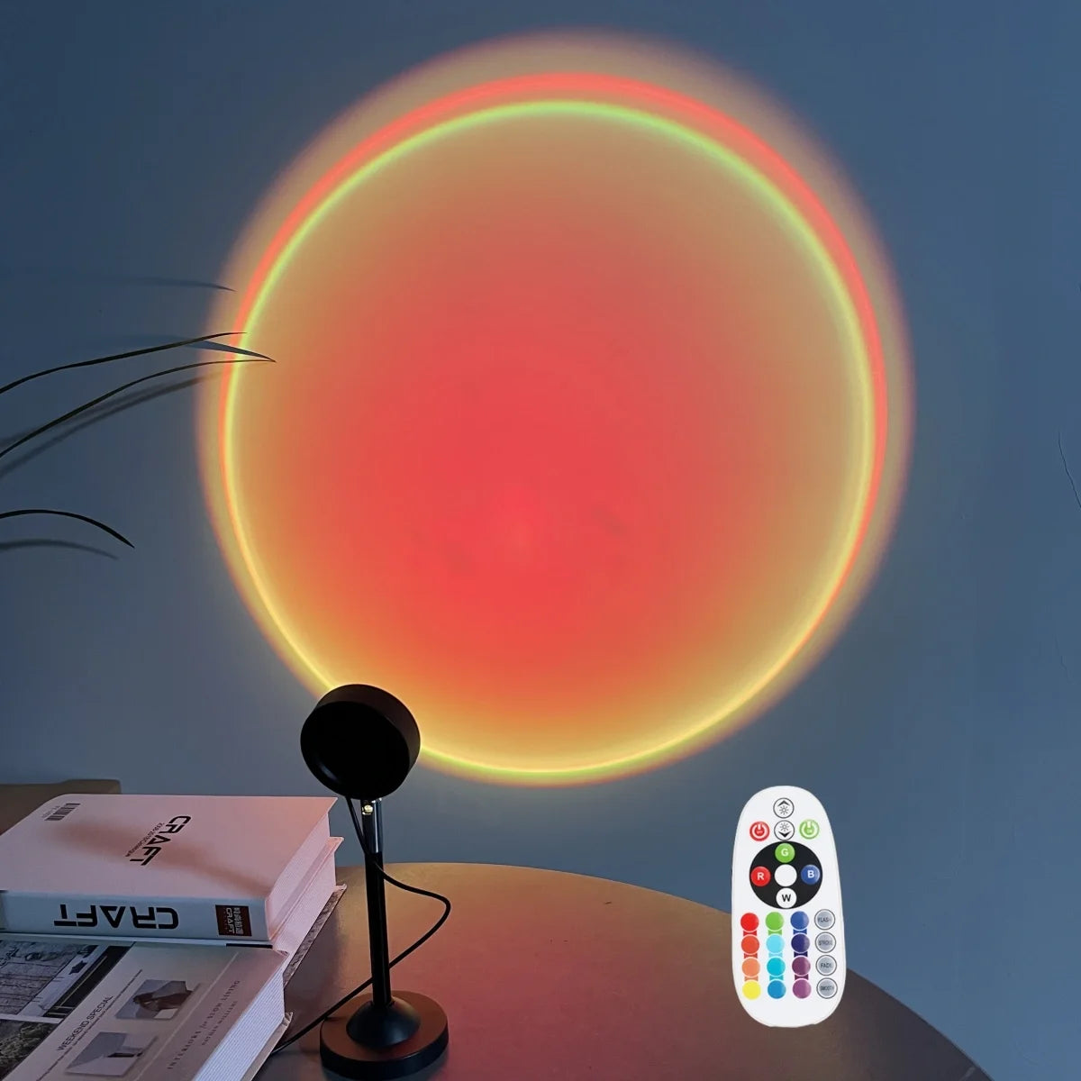 A USB sunset projection light is shown illuminating a wall with a bright orange glow, next to a remote control and some books