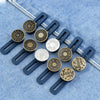 Six dark blue and brass button waist extenders for jeans displayed on a light blue denim fabric.