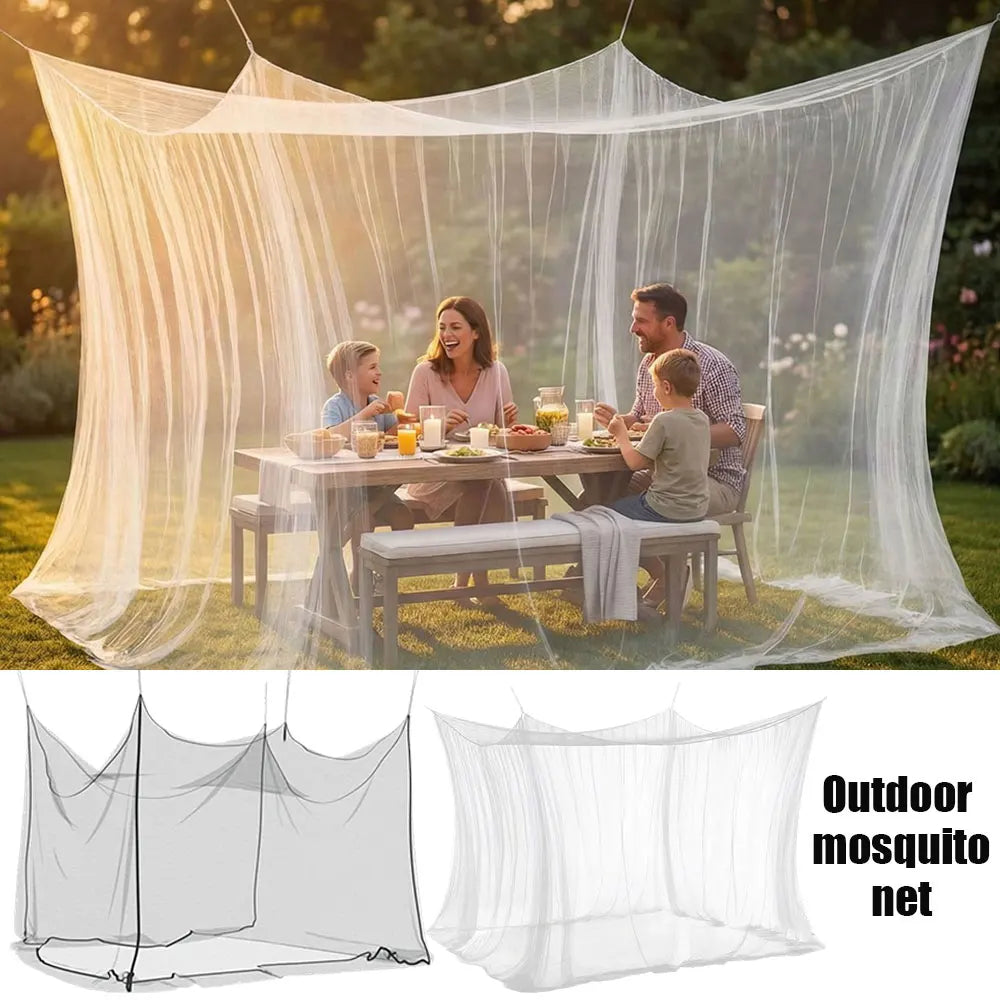A large white mesh mosquito net canopy is set up outdoors, draped over a wooden table where a family is having a meal.