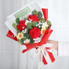 Ein Strauß aus roten und weißen handgefertigten Häkelblumen mit grünen Blättern, in ropem Papier eingewickelt.