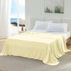 A light yellow ice silk blanket is draped over a bed in a bright bedroom setting.