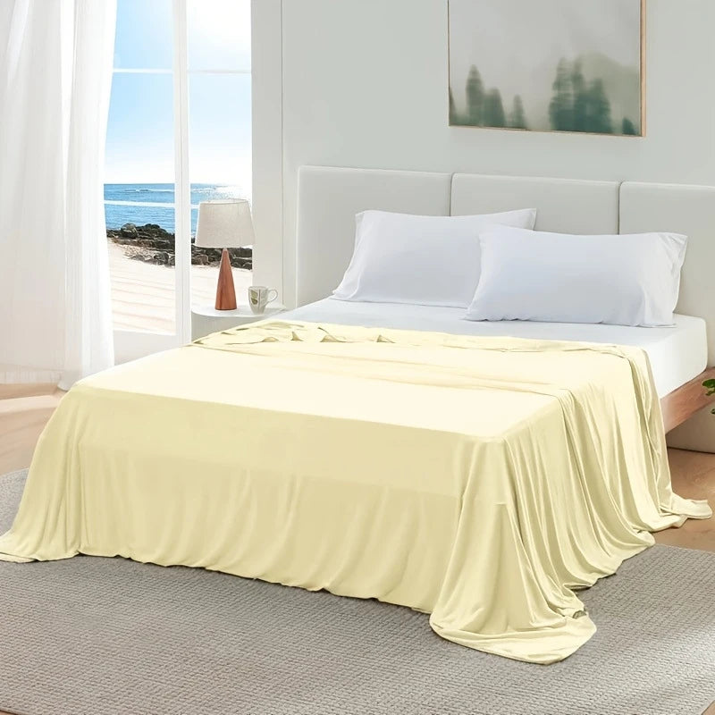 A light yellow ice silk blanket is draped over a bed in a bright bedroom setting.