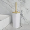 A tall white toilet brush set with a gold rotating stand is shown next to a white bathtub.