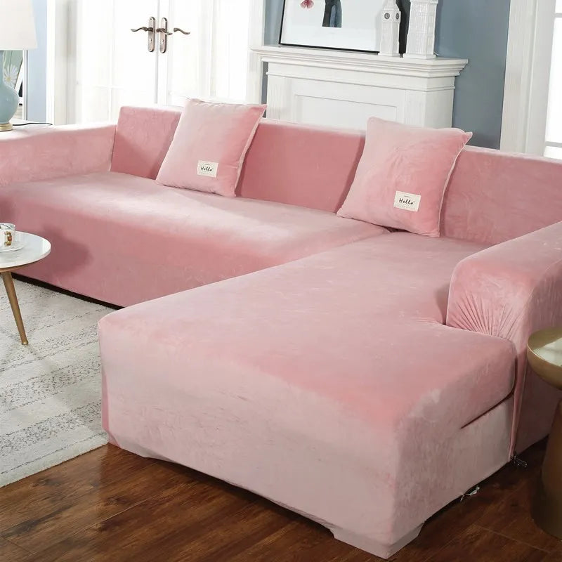 A pink plush velvet elastic sofa cover with pillows is shown on an L-shaped sofa in a bright room.