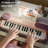 A child plays a pink electronic piano with 37 black and white keys, surrounded by instructional cards.