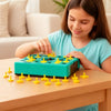 A young girl is playing with a green shape matching puzzle game on a wooden table.