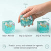 A hand is shown pressing a translucent blue sea shell cube, illustrating a three-step process for a gentle tactile sensory ex