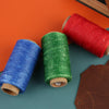 Three spools of waxed polyester thread in red, green, and blue lying on a dark surface.