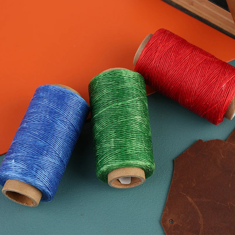 Three spools of waxed polyester thread in red, green, and blue lying on a dark surface.