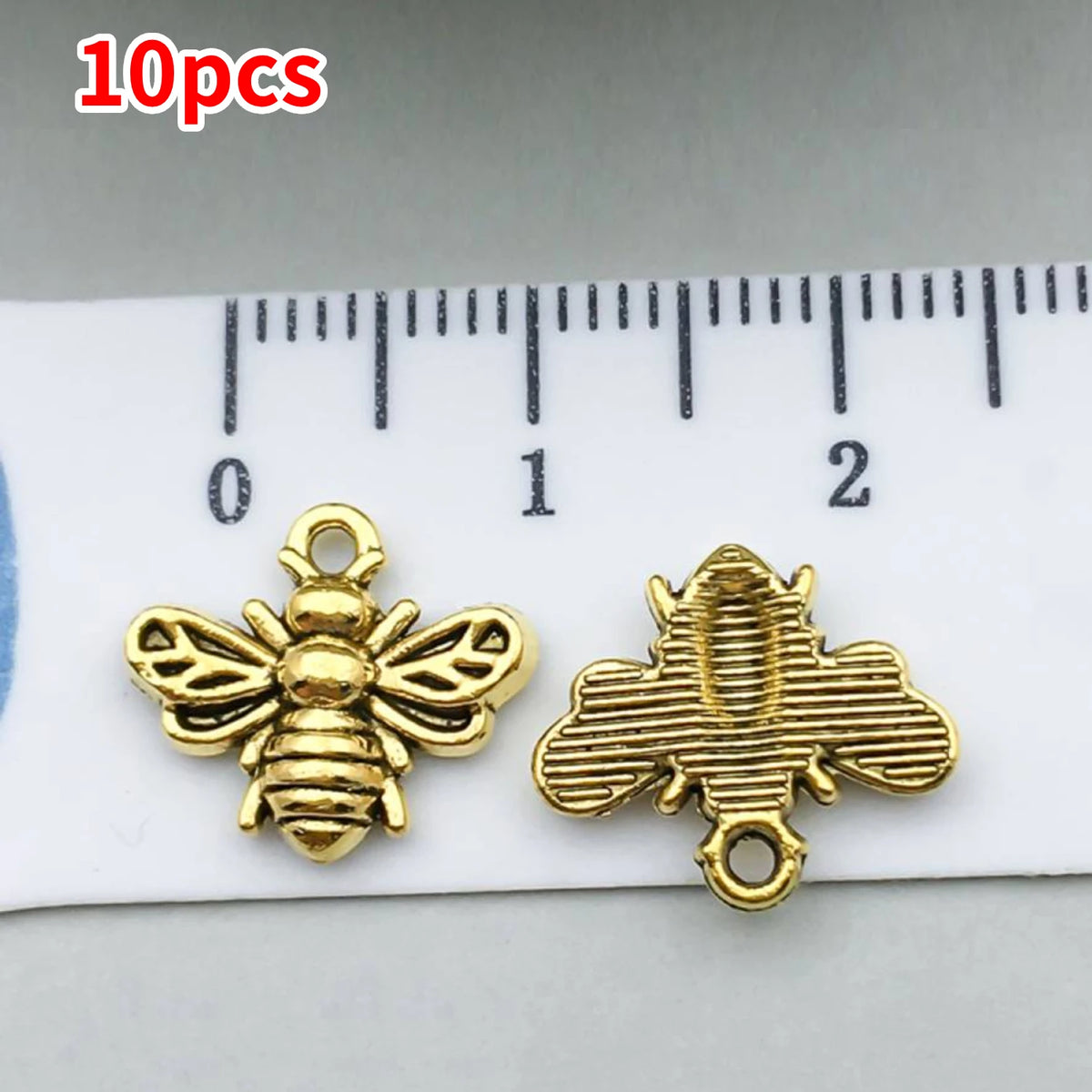 10 pieces of gold-colored bee and sunflower charm pendants displayed next to a ruler.