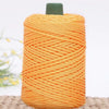 A spool of bright orange crochet ice rope with a dark green cap, lying on a woven surface.