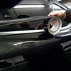 A hand is applying a glossy black vinyl wrap strip to the trim of a dark car.