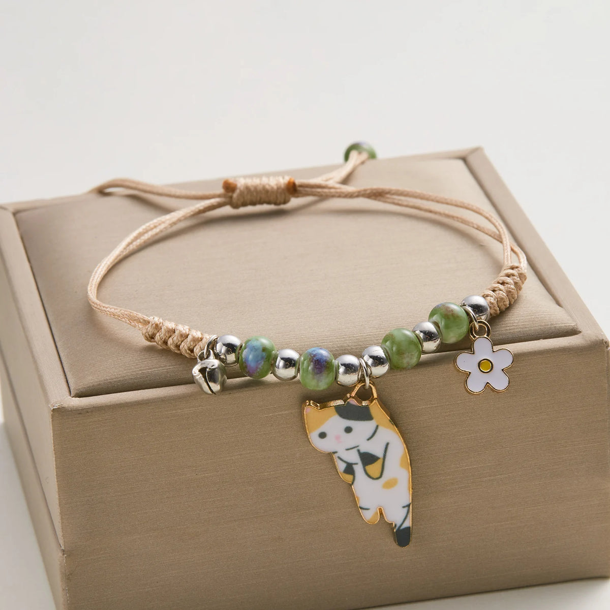 Armband mit Perlenkette in grün- und blauen Steinen und einem Anhänger in Form einer weißen Katze und Blume