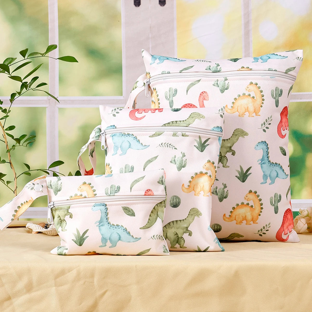 A set of reusable waterproof wet bags featuring various dinosaur patterns in green, yellow, and pink on a light background.
