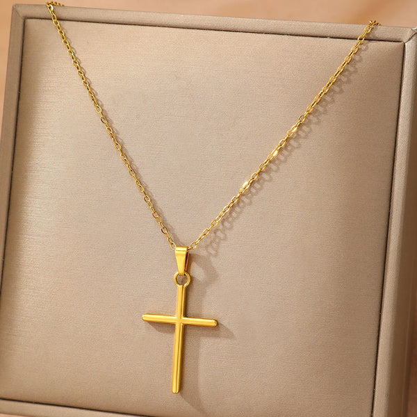 A gold-colored stainless steel cross pendant necklace displayed on a light brown box.