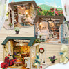 A wooden miniature dollhouse kit with interior details and LED lights displayed on a light wood surface.