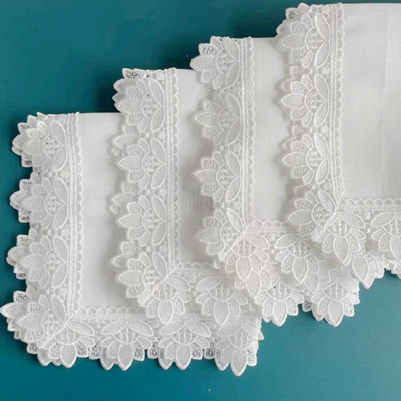 A set of six white linen hemstitch napkins with delicate lace trim displayed on a teal surface.