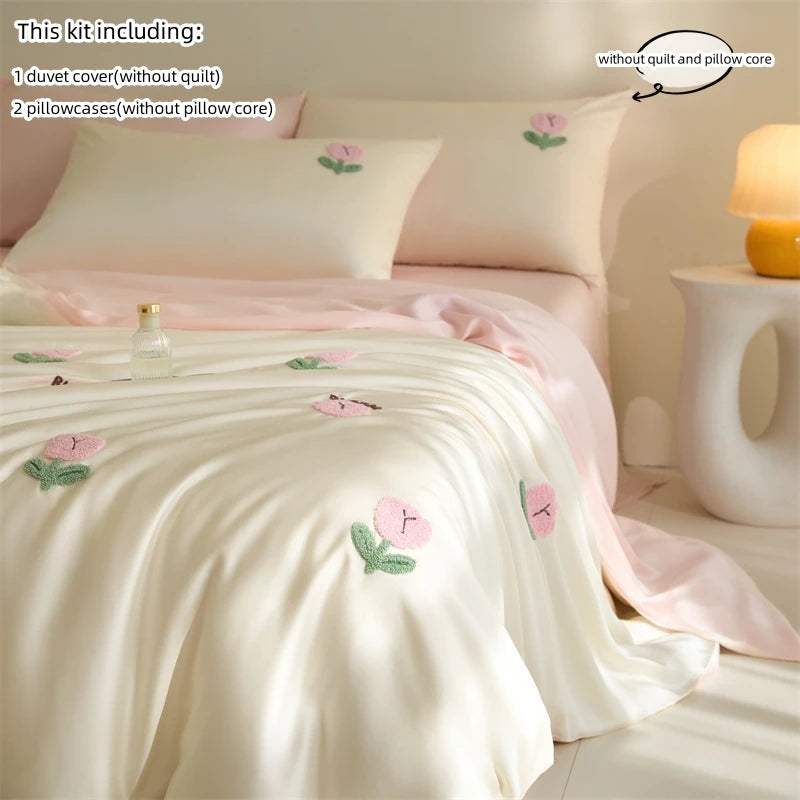 A set of embroidered tulip duvet cover and pillowcases in soft pink and cream colors displayed on a bed.