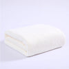A stack of white plush coral velvet bath towels folded neatly on a white surface.